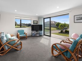 A living room with rattan armchairs and a sofa with cushions a television on a stand and sliding glass door at Bennett's Bach - Waipu Holiday Home in Waipu