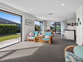 An open living and dining area with rattan chairs and a dining table next to large sliding glass doors at Bennett's Bach - Waipu Holiday Home in Waipu