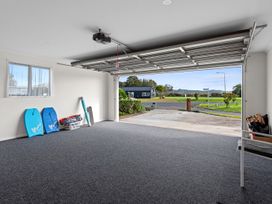 A garage with an open door showing a driveway outside and bodyboards and a laundry basket inside at Bennett's Bach - Waipu Holiday Home in Waipu