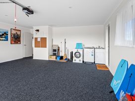 A laundry room with washing machines cleaning tools and two blue bodyboards leaning against the wall at Bennetts Bach Waipu Holiday Home Waipu