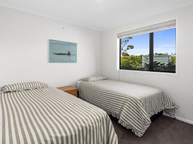 A bedroom with two single beds with striped bedding a wooden nightstand and a window showing greenery at Bennett's Bach - Waipu Holiday Home in Waipu