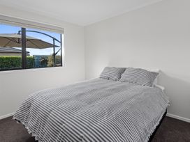 A bedroom with a bed made with striped bedding and a window showing outdoor umbrella at Bennett's Bach - Waipu Holiday Home in Waipu