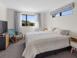 A bedroom with a large bed two bedside tables a chair a television and two windows with curtains at Bennett's Bach - Waipu Holiday Home in Waipu