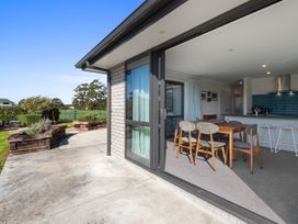 Dining area with wooden table and chairs next to kitchen with bar stools and open sliding door to outdoor patio at Bennetts Bach Waipu Holiday Home Waipu