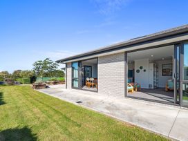Exterior view of a single-story house with sliding glass doors opening to a grassy backyard at Bennett's Bach - Waipu Holiday Home in Waipu