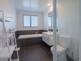 A bathroom with a bathtub under a window a floating vanity with sink a toilet and a white shelving unit at Bennetts Bach - Waipu Holiday Home in Waipu