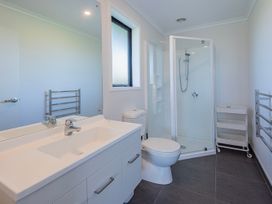 A bathroom with a white sink and cabinet a toilet a shower with glass door a window a towel rack and a storage cart on wheels at Bennett's Bach - Waipu Holiday Home in Waipu