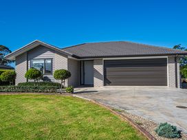 A one-story house with a grey tiled roof a double garage a small front yard with trimmed bushes and green grass at Bennetts Bach - Waipu Holiday Home in Waipu