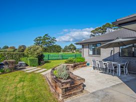 An outdoor patio with a dining table and chairs under an umbrella next to a house with a garden and lawn at Bennett's Bach - Waipu Holiday Home in Waipu