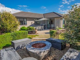 An outdoor seating area with benches and a firepit in a garden with bushes and stone steps leading to a patio with a dining table and umbrella at Bennett's Bach - Waipu Holiday Home in Waipu