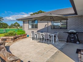 An outdoor patio with a table and six chairs under a large umbrella and a barbecue grill outside Bennett's Bach - Waipu Holiday Home in Waipu