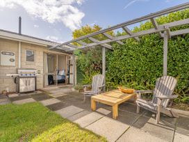 An outdoor patio area with two wooden chairs a wooden table a barbecue grill and a pergola at Boulevard Bliss - Pauanui Holiday Home in Pauanui