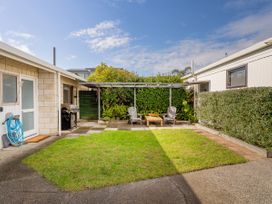 A backyard with a small lawn patio area two chairs and a table under a pergola with a barbecue grill near a house at Boulevard Bliss - Pauanui Holiday Home in Pauanui