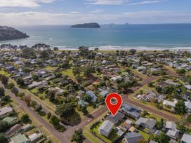 A coastal residential neighborhood with houses trees and roads near a beach and ocean with an island in the distance at Boulevard Bliss - Pauanui Holiday Home in Pauanui