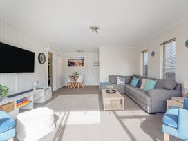 A living room with a gray sectional sofa cushions a wooden coffee table and a dining table with white chairs at Boulevard Bliss - Pauanui Holiday Home in Pauanui