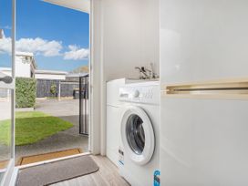A laundry room with a washing machine a sink an open door leading outside at Boulevard Bliss - Pauanui Holiday Home in Pauanui