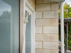 A wall-mounted shower head attached to an exterior door frame with a gutter pipe and garden visible behind the brick wall at Boulevard Bliss - Pauanui Holiday Home in Pauanui