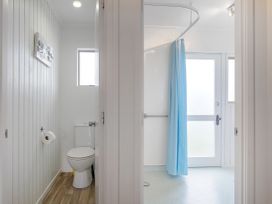 A bathroom with a toilet on the left and a shower with a blue curtain on the right at Boulevard Bliss Pauanui Holiday Home in Pauanui