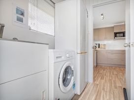 A laundry area with a washing machine, sink, and refrigerator leading into a kitchen with cabinets and a microwave at Boulevard Bliss - Pauanui Holiday Home in Pauanui