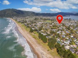 An aerial view of a coastal town with a beach and houses marked with a location pin at Boulevard Bliss - Pauanui Holiday Home in Pauanui