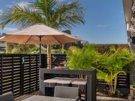 An outdoor patio area with a table and chairs a bar table with stools a large umbrella and palm plants at Boulevard Bliss - Pauanui Holiday Home in Pauanui
