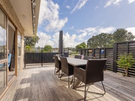 An outdoor patio with a dining table and chairs on a wooden deck at Boulevard Bliss Pauanui Holiday Home in Pauanui