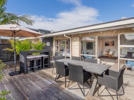 An outdoor wooden deck with a dining table and chairs an umbrella and a bar table with stools at Boulevard Bliss Pauanui Holiday Home in Pauanui
