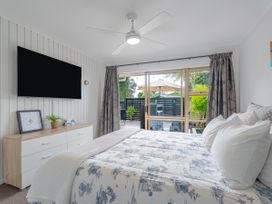 A bedroom with a bed a dresser a ceiling fan and a sliding glass door opening to an outdoor patio at Boulevard Bliss - Pauanui Holiday Home in Pauanui