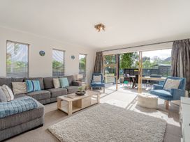 A living room with a grey sectional sofa, blue armchairs, a wooden coffee table, and sliding glass doors to a deck at Boulevard Bliss - Pauanui Holiday Home in Pauanui