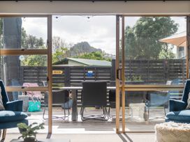 A dining table with chairs on a patio seen through glass sliding doors with blue armchairs inside at Boulevard Bliss - Pauanui Holiday Home in Pauanui
