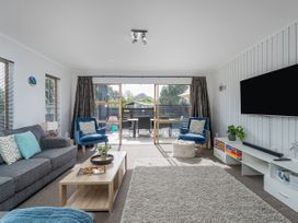 A living room with gray sofa blue chairs coffee table and large tv at Boulevard Bliss - Pauanui Holiday Home in Pauanui