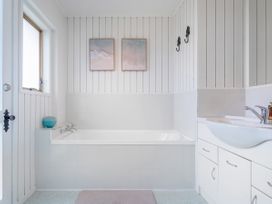 A bathroom with a bathtub sink and cabinet with two paintings on the wall at Boulevard Bliss - Pauanui Holiday Home in Pauanui