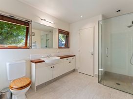 A bathroom with a toilet with wooden seat a sink with wooden countertop a large mirror a glass shower enclosure and two windows at Peaceful Outlook - Hatepe Holiday Home in Hatepe
