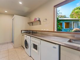A laundry room with washing machine dryer mini fridge and a window showing a blue house outside at Peaceful Outlook - Hatepe Holiday Home in Hatepe