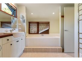 A bathroom with a large bathtub below a window with wooden blinds and a sink with cabinets and a mirror Peaceful Outlook - Hatepe Holiday Home in Hatepe