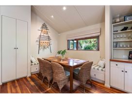 A dining area with a wooden table surrounded by wicker chairs and bench seating with cushions by a window with a wall decoration Peaceful Outlook - Hatepe Holiday Home Hatepe