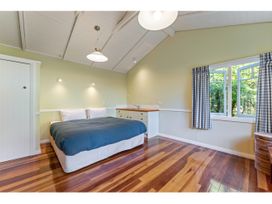 A bedroom with a bed a sink with cabinets wooden floor and an open window with blue check curtains at Peaceful Outlook Hatepe Holiday Home in Hatepe