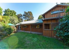 A wooden house with a green lawn and surrounding trees at Peaceful Outlook - Hatepe Holiday Home in Hatepe