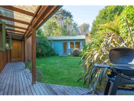A backyard with a wooden deck, a blue shed, green grass, plants, and a barbecue at Peaceful Outlook - Hatepe Holiday Home in Hatepe