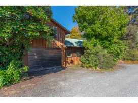 A brown wooden house with a garage door surrounded by trees and shrubs at Peaceful Outlook - Hatepe Holiday Home in Hatepe