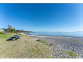 A beach with a picnic table grassy area shoreline and distant trees at Peaceful Outlook - Hatepe Holiday Home in Hatepe