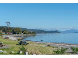 A coastline with a picnic table on grass near a pebble beach and calm water at Peaceful Outlook - Hatepe Holiday Home in Hatepe
