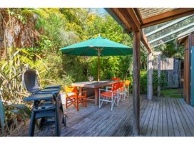 An outdoor patio with a wooden table under a green umbrella surrounded by orange and white chairs and a black barbecue grill at Peaceful Outlook - Hatepe Holiday Home in Hatepe