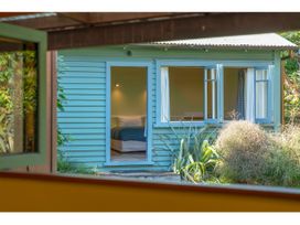 A view of a blue wooden house with an open door showing a bed inside and open windows with plants outside at Peaceful Outlook - Hatepe Holiday Home in Hatepe
