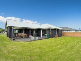 A single story house with dark brick walls and a light roof next to a grassy lawn with outdoor chairs on a patio at Tide and Tranquility Whitianga