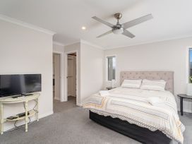 A bedroom with a bed two bedside tables a ceiling fan and a TV on a small table at Tide and Tranquility - Whitianga Holiday Home in Whitianga