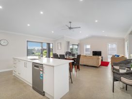 An open plan kitchen and living area with a white island bench a dining table with chairs sofas and a television at Tide and Tranquility - Whitianga Holiday Home in Whitianga