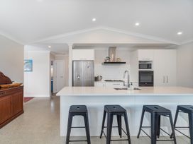A kitchen with a white island and four black stools a silver refrigerator an oven a microwave and a wooden sideboard at Tide and Tranquility - Whitianga Holiday Home in Whitianga
