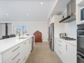 A kitchen with white cabinets an island with a sink a gas stove a stainless steel refrigerator and a wooden cabinet at Tide and Tranquility - Whitianga Holiday Home