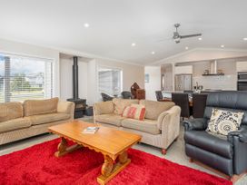 A living room with beige sofas a black leather chair a wooden coffee table and a red rug at Tide and Tranquility in Whitianga